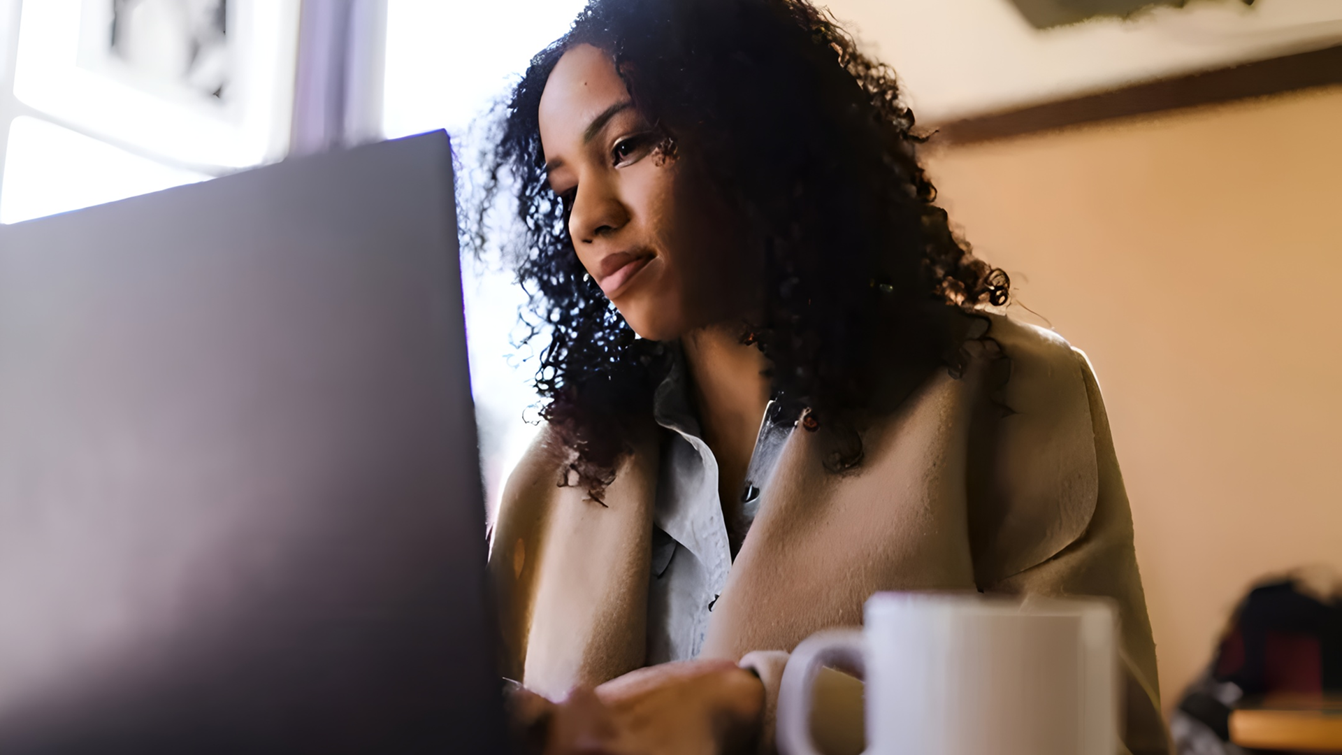 Woman working on laptop with coffee mug.