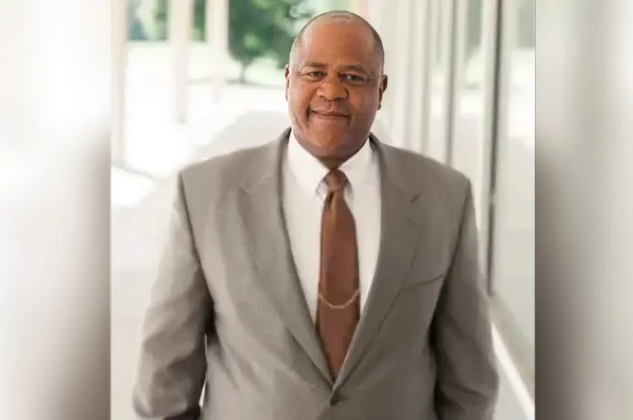 Man in suit standing near glass windows.